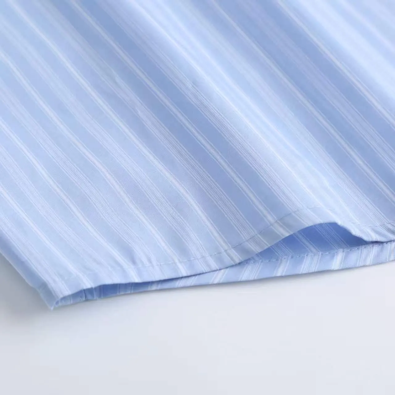 AMI Embroidered Striped Shirt Fabric Selection: Made of 100% cotton poplin fabric. The pure cotton fiber can quickly absorb moisture and perspire, making it refreshing and not stuffy when worn for a long time. The unique plain weave process of poplin makes the fabric both soft and skeletal, not easy to wrinkle and deform, and the upper body is neat and clean. Coupled with the fine blue and white stripes all over the body, the light color scheme is gentle and elegant, which can meet the needs of different scenes. Process 1: Accurately mark the embroidery position on the chest patch pocket to ensure that the pattern does not shift and does not destroy the overall beauty of the striped fabric. High-count embroidery threads of the same color as the fabric are selected, and flat stitch embroidery technology is used. The stitches are evenly tracked, the edges are clean and neat, and the love outline is simple and smooth. It retains recognition without irritating the skin. It is blended into the striped texture in a low-key manner to avoid an abrupt feeling, while ensuring that the embroidery threads are Wear-Resistant. 2: After the embroidery is completed, perform high-temperature ironing and thread trimming to ensure that the pattern is smooth and compliant, and it is not easy to lose thread or warp after being worn for a long time. Details: 1. The collar seat adopts double-layer reinforcement technology, which is not easy to collapse and deform after long-term wear. The collar corner has a soft arc, which can modify the neck line without being too sharp, making it neat and decent. 2. The inner side of the placket has hidden hemming treatment to avoid burrs on the fabric, while enhancing structural stability and preventing it from deforming after multiple washes. Accessories: One-to-one customized buttons Size: S M L XL Style number: D 236